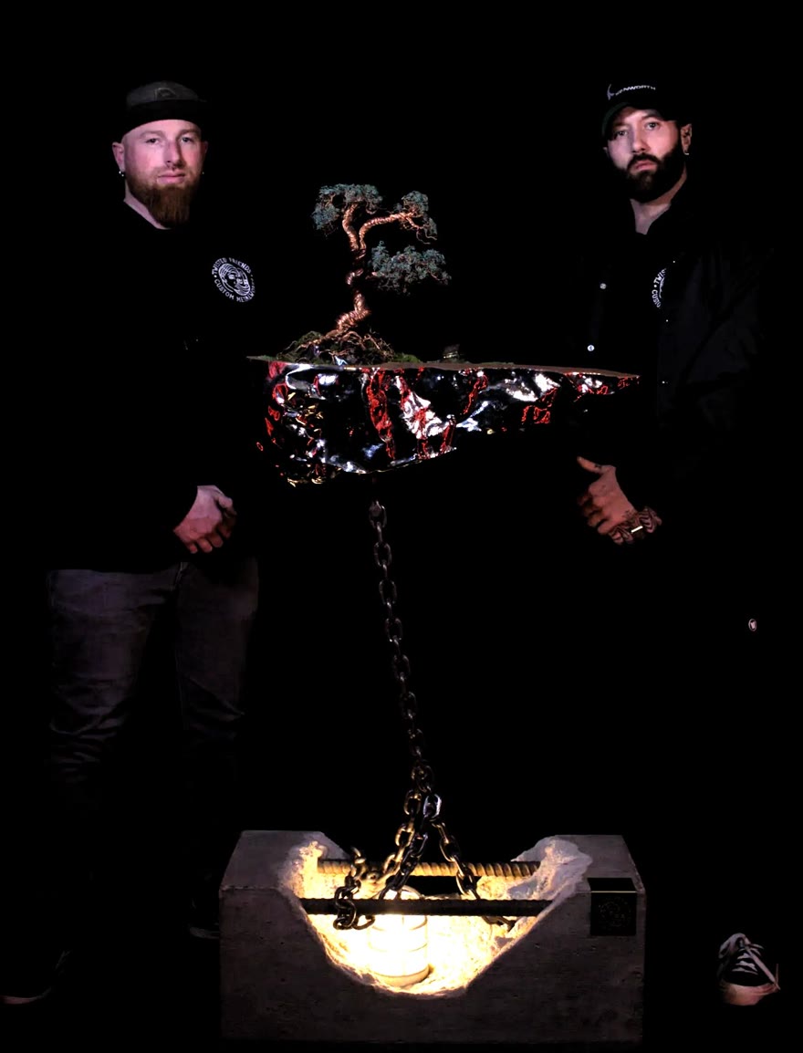 The two makers behind Twisted Friends holding a suspended island sculpture